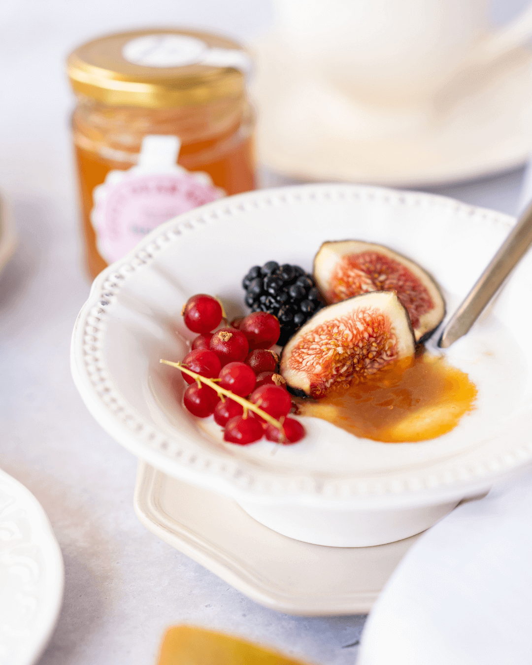 Weiße Porzellanschüssel mit Joghurt, frischen Feigen, Johannisbeeren, Brombeeren und "Tangerine Love" Konfitüre.