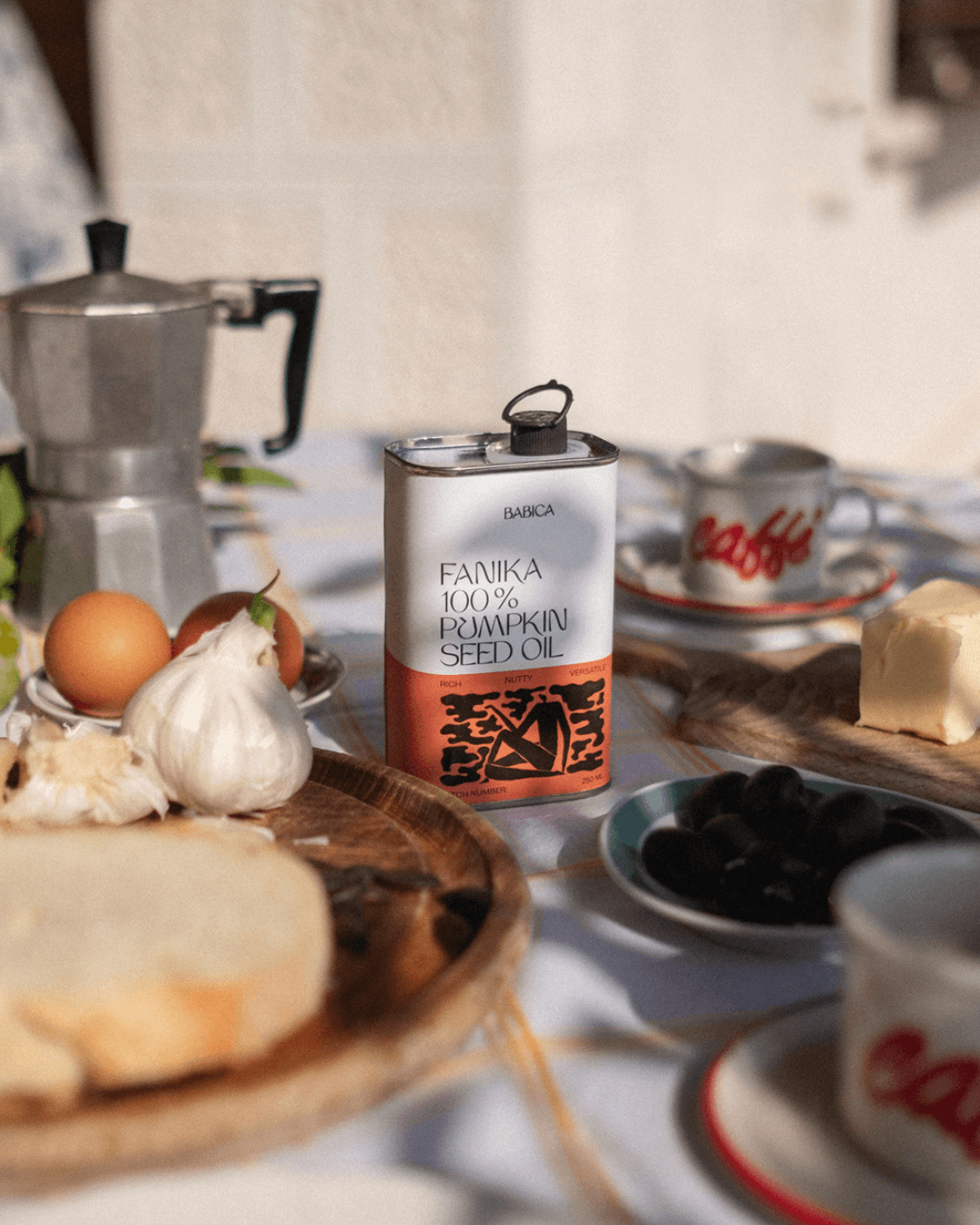 Frühstückstisch bei Sonnenschein mit Babica Fanika 100% Kürbiskernöl, Brot, Knoblauch, Butter, Eiern, Oliven und Kaffee.