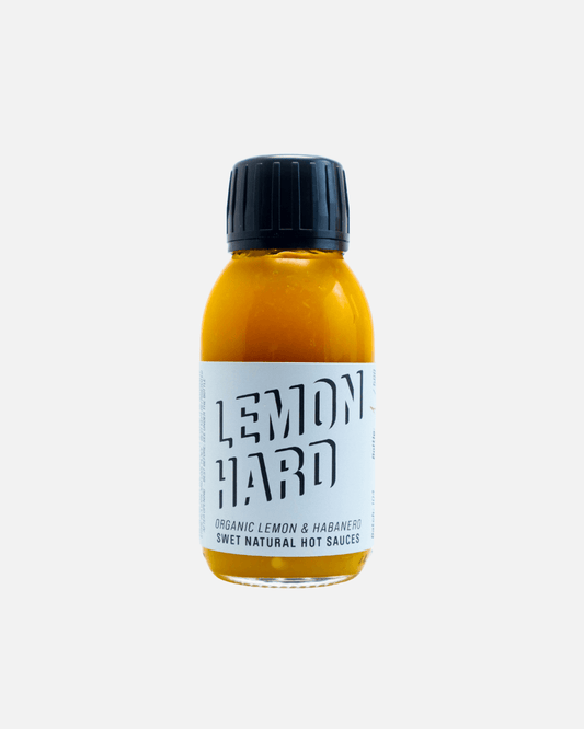 Eine durchsichtige Glasflasche mit SWET „Lemon Hard“ Hot Sauce, die Sauce in fruchtiger gelber Farbe.