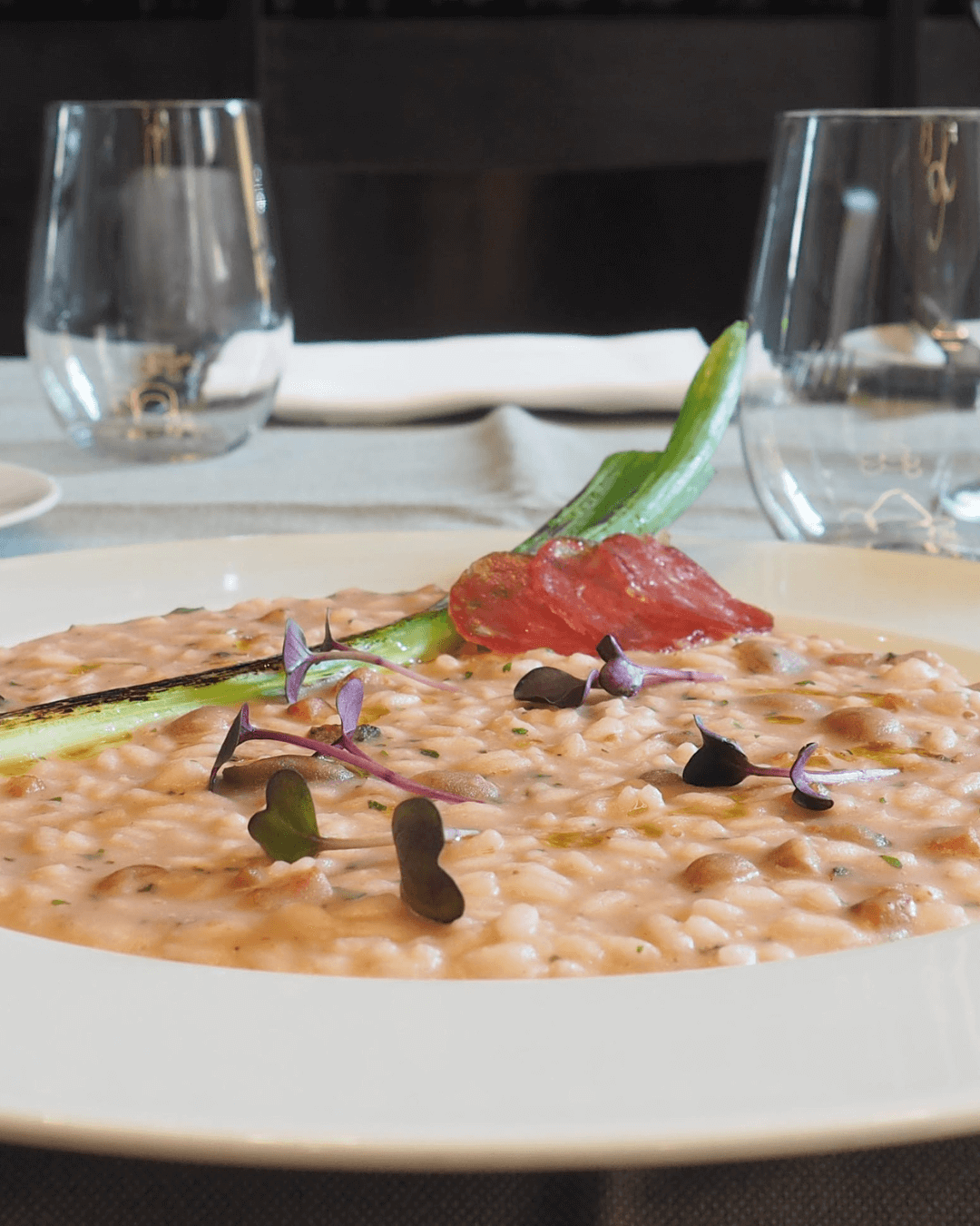 Cremiges Risotto mit Gemüse und Microgreens auf weißem Teller serviert.