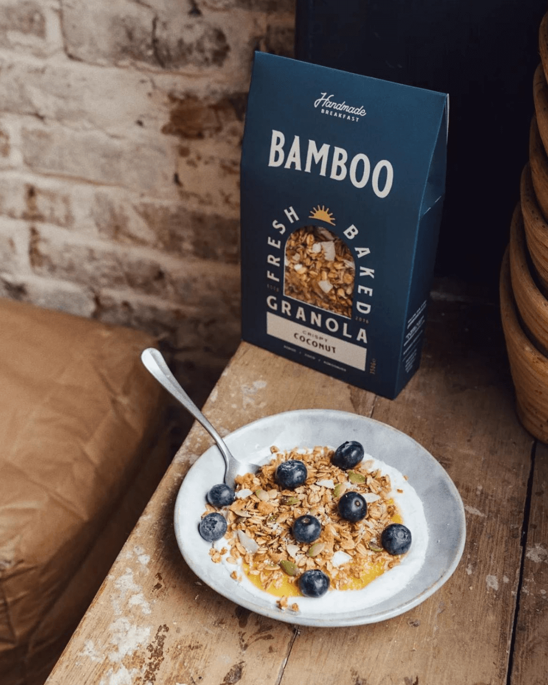 Ein Tisch mit einer Schüssel Bamboo Breakfast Granola mit knusprigen Kokosflocken, Blaubeeren und Joghurt.
