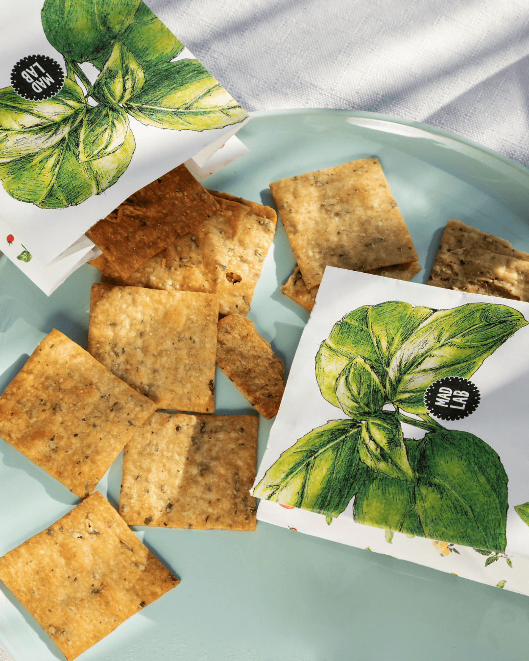 Knusprige Bio-Cracker mit Tomaten und Basilikum von Mad Lab, stilvoll arrangiert auf hellblauem Teller.