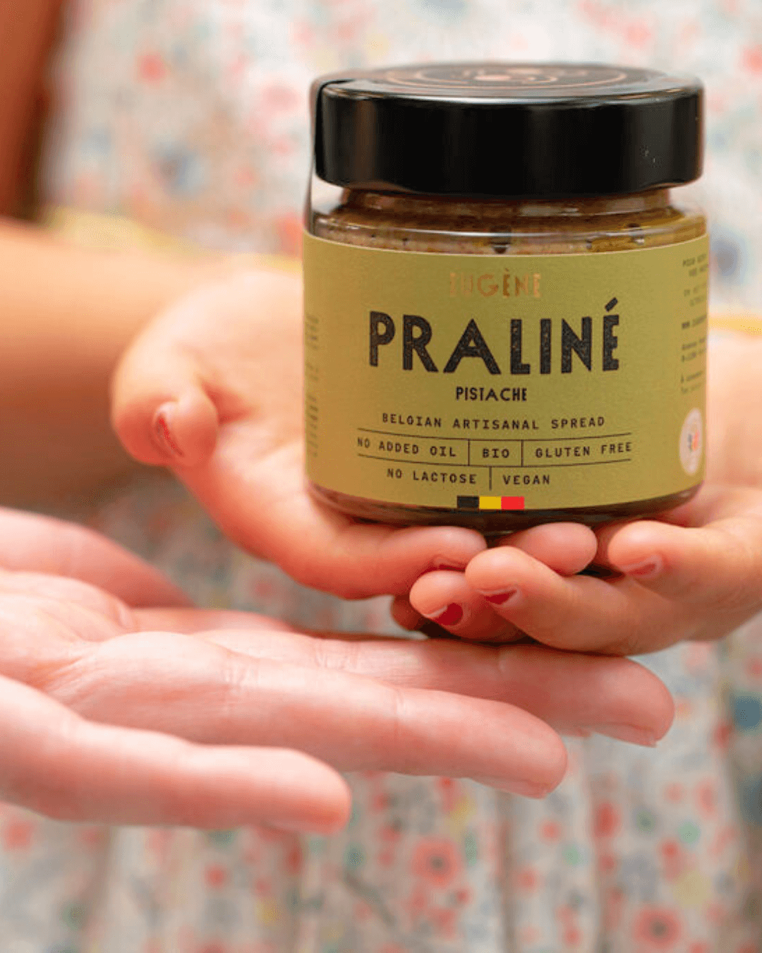 Bio-Praliné Pistazienaufstrich von Eugène Chocolatier wird mit zwei Händen weitergereicht.