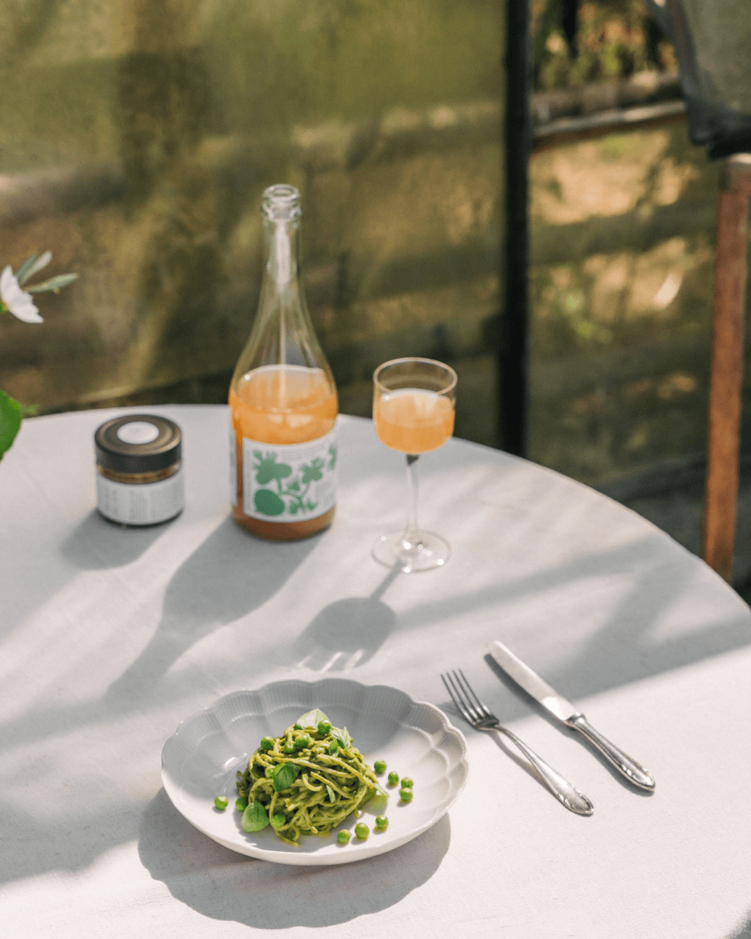 Flasche Bouche Melone Szechuan Pet Nat Kombucha auf einem sonnigen Tisch mit einem Glas und einem Teller Pasta.