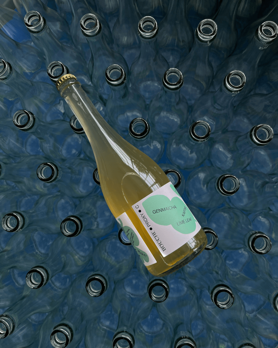 Flasche Bouche Proxy C mit Genmaicha und Kaffir-Limettenblättern auf einem Bett aus leeren Glasflaschen.