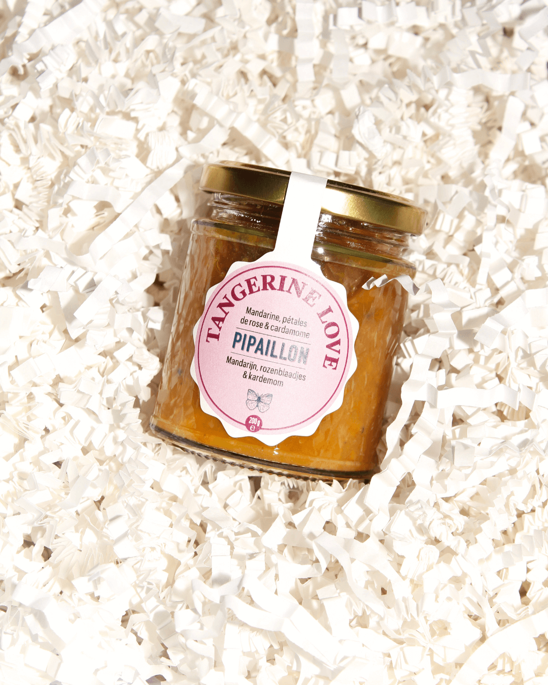 Ein Glas „Tangerine Love“-Marmelade von Pipaillon, arrangiert auf weißem Papierfüllmaterial in einer Geschenkbox.