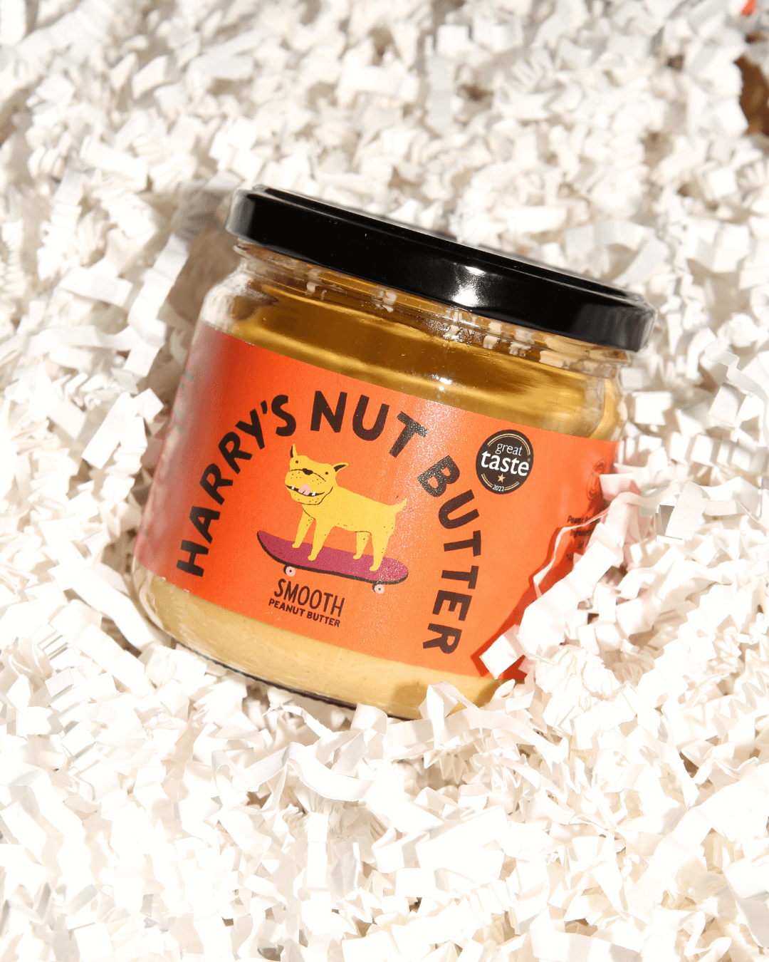 Ein Glas „Harry’s Nut Butter Smooth“ Erdnussbutter, arrangiert auf weißem Papierfüllmaterial in einer Geschenkbox.