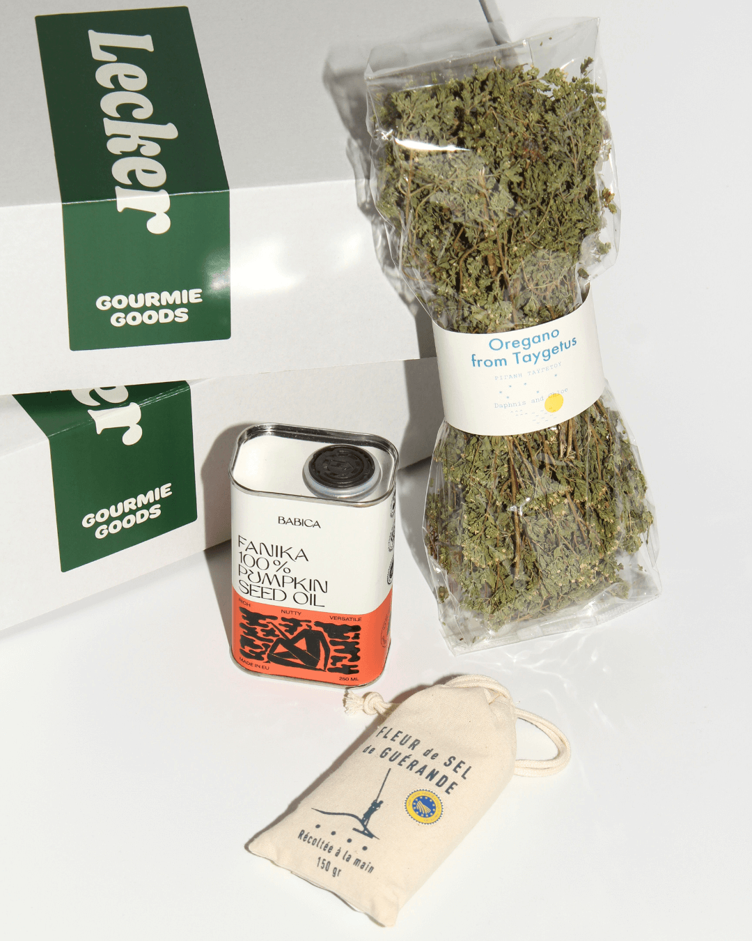 Produkte aus dem Geschenkset "Chef’s Secret Stash" neben der Box: Kürbiskernöl, Fleur de Sel, getrockneter Oregano.