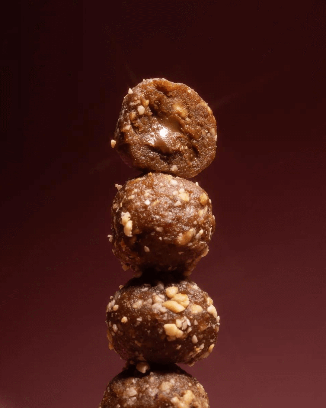 Ein Stapel Cravers Crunchy Haselnuss-Energiekugeln, Nahaufnahme mit sichtbarer Füllung, vor einem dunkelroten Hintergrund.