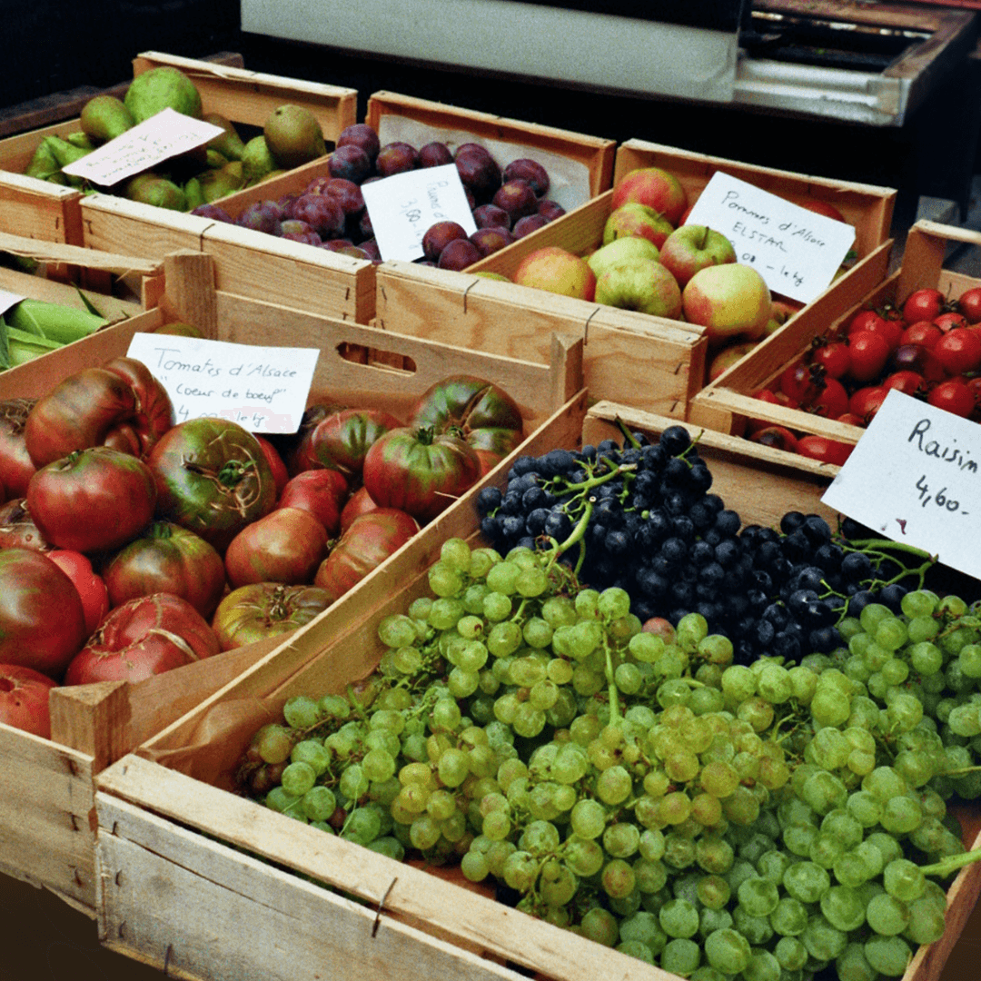 Frisches Obst und Gemüse auf einem Bauernmarkt – Tomaten, Trauben, Äpfel und Pflaumen in Holzkisten.