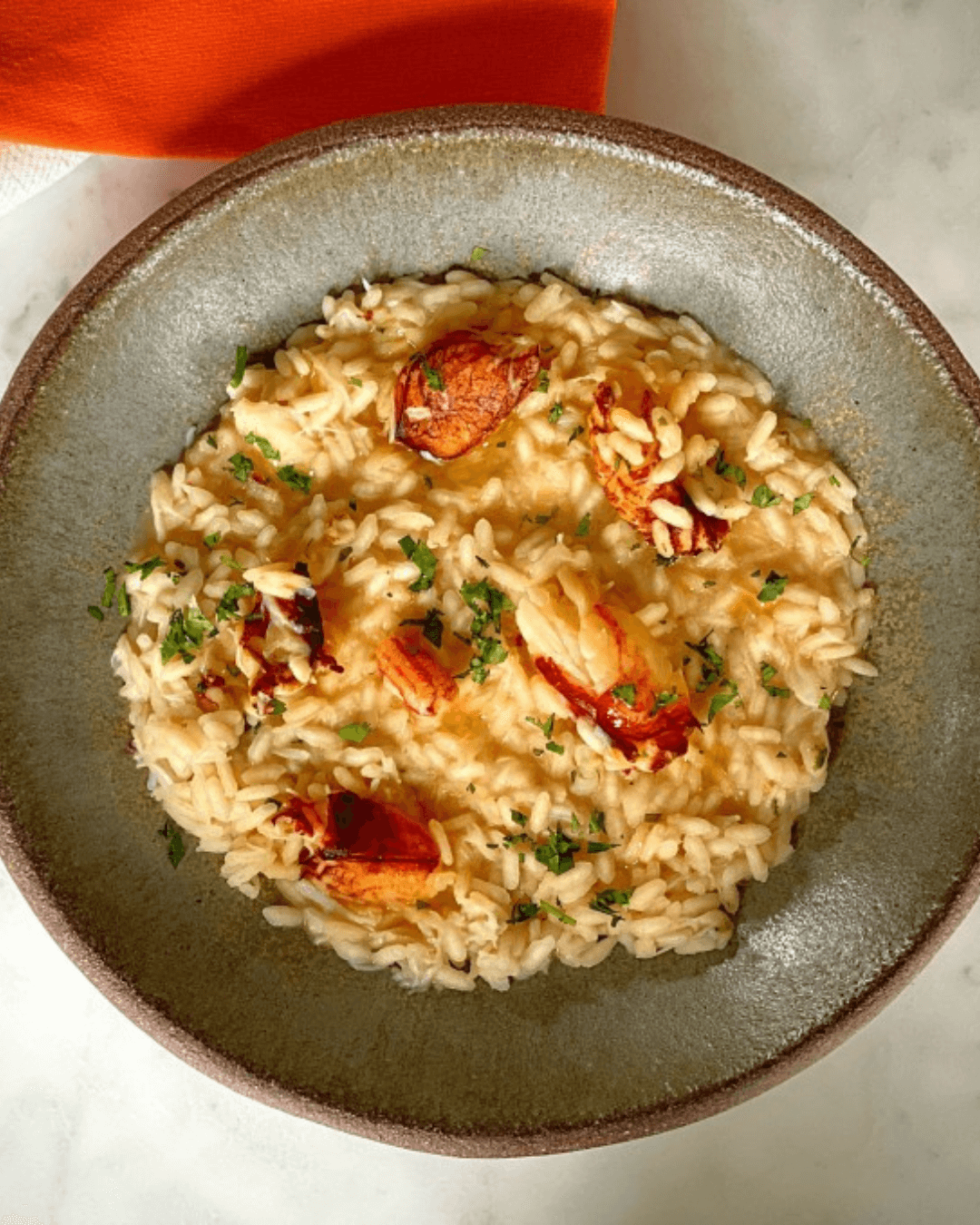 Cremiges Risotto mit Acquerello Carnaroli Reis und Hummerstücken, serviert in einer Keramikschale und mit frischen Kräutern garniert.