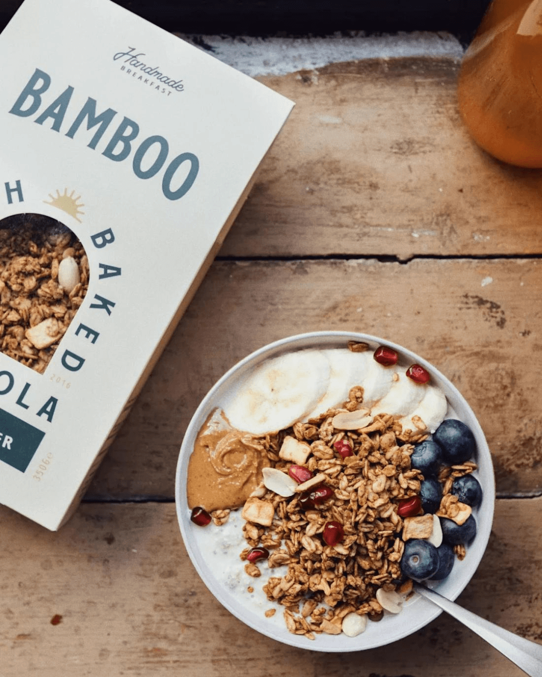 Eine Schale mit Bamboo Breakfast Granola mit Erdnussbutter & Apfel, Banane und Heidelbeeren, daneben die Granola-Packung.