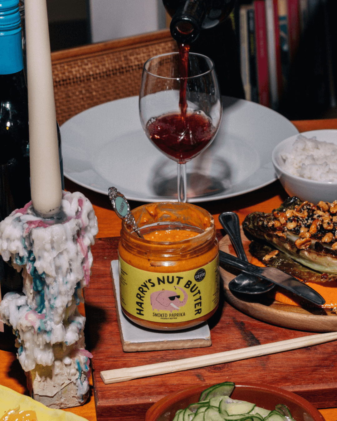 Tisch mit Speisen, Kerze, Wein, Salat, gegrilltem Gemüse, und "Harry's Nut Butter" mit geräuchertem Paprika im Vordergrund.