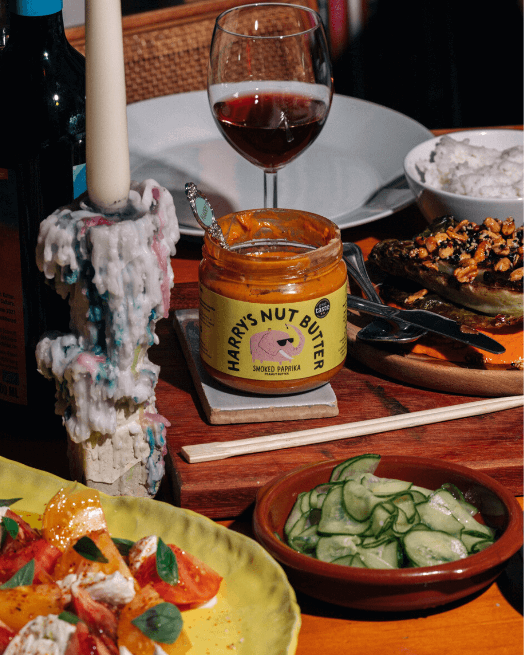 Ein gemütlicher Esstisch mit Rotwein, Kerze, Harry's Nut Butter Erdnussbutter mit geräuchertem Paprika, Salat, Gurken, Reis.