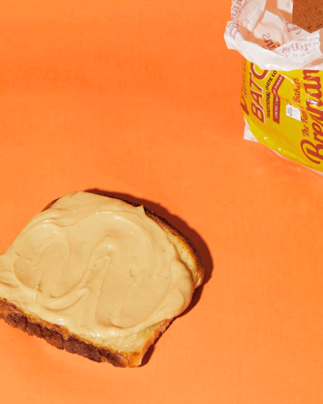 Ein Stück Toast mit einer dicken Schicht Harry's Nut Butter Smooth Erdnussbutter, daneben eine Packung Brot.