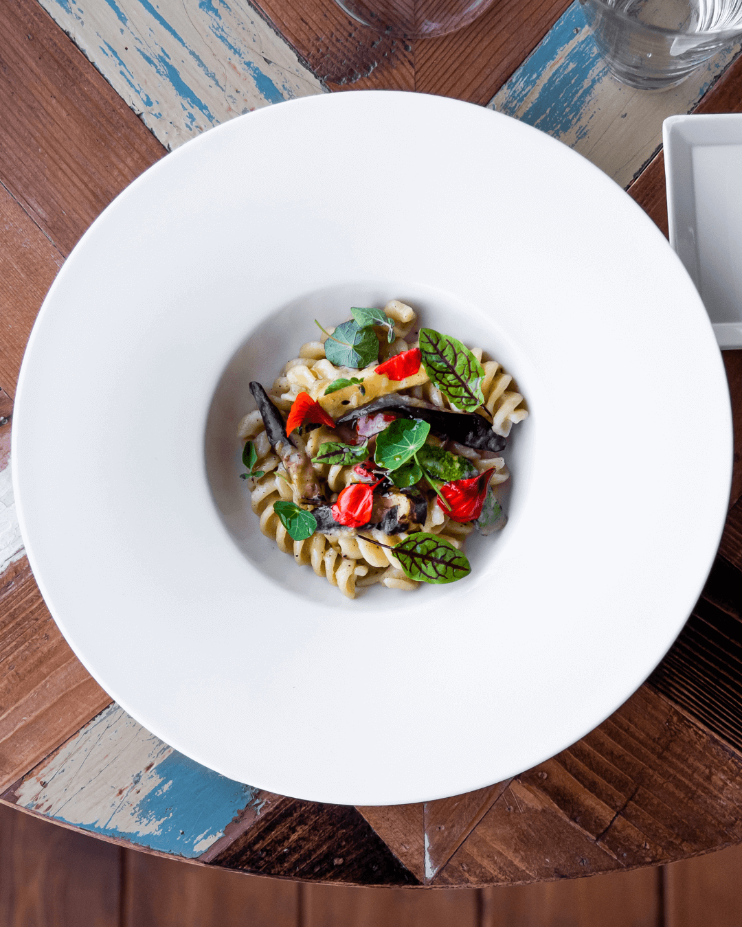 Fusilli mit gegrilltem Gemüse und frischen Kräutern auf modernem weißen Teller.