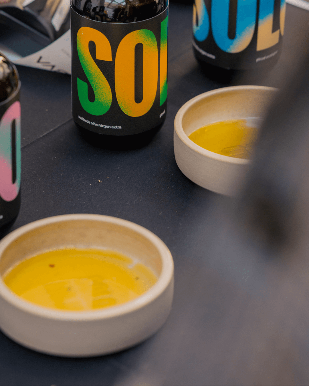 Verschiedene Flaschen mit nativem Olivenöl extra von SOLO, zwei Teller mit lebhaftem, goldfarbenem Olivenöl auf einem Tisch.