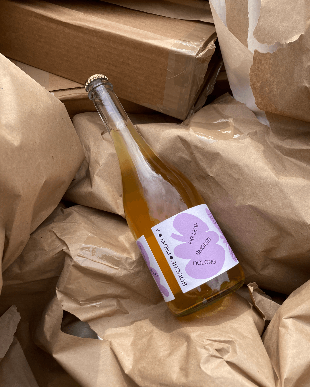 Eine Flasche Proxy A von Bouche mit einem rosafarbenen Etikett liegt auf einem Stapel braunen Verpackungspapiers.
