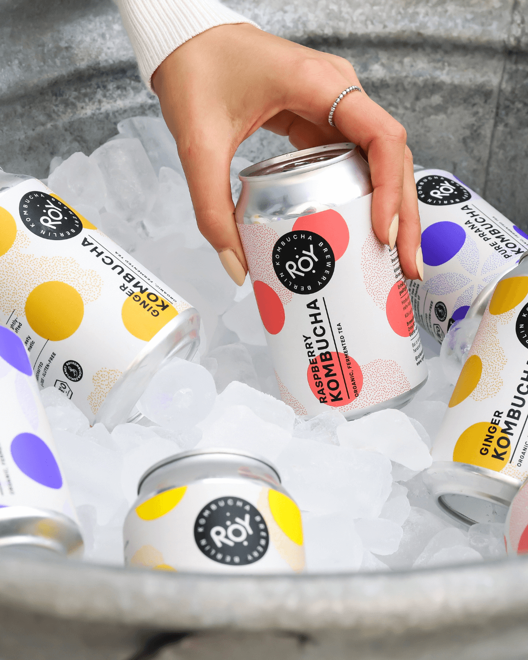 Hand greift nach einer Dose Roy Kombucha Raspberry aus einem Eiskübel mit verschiedenen Sorten.