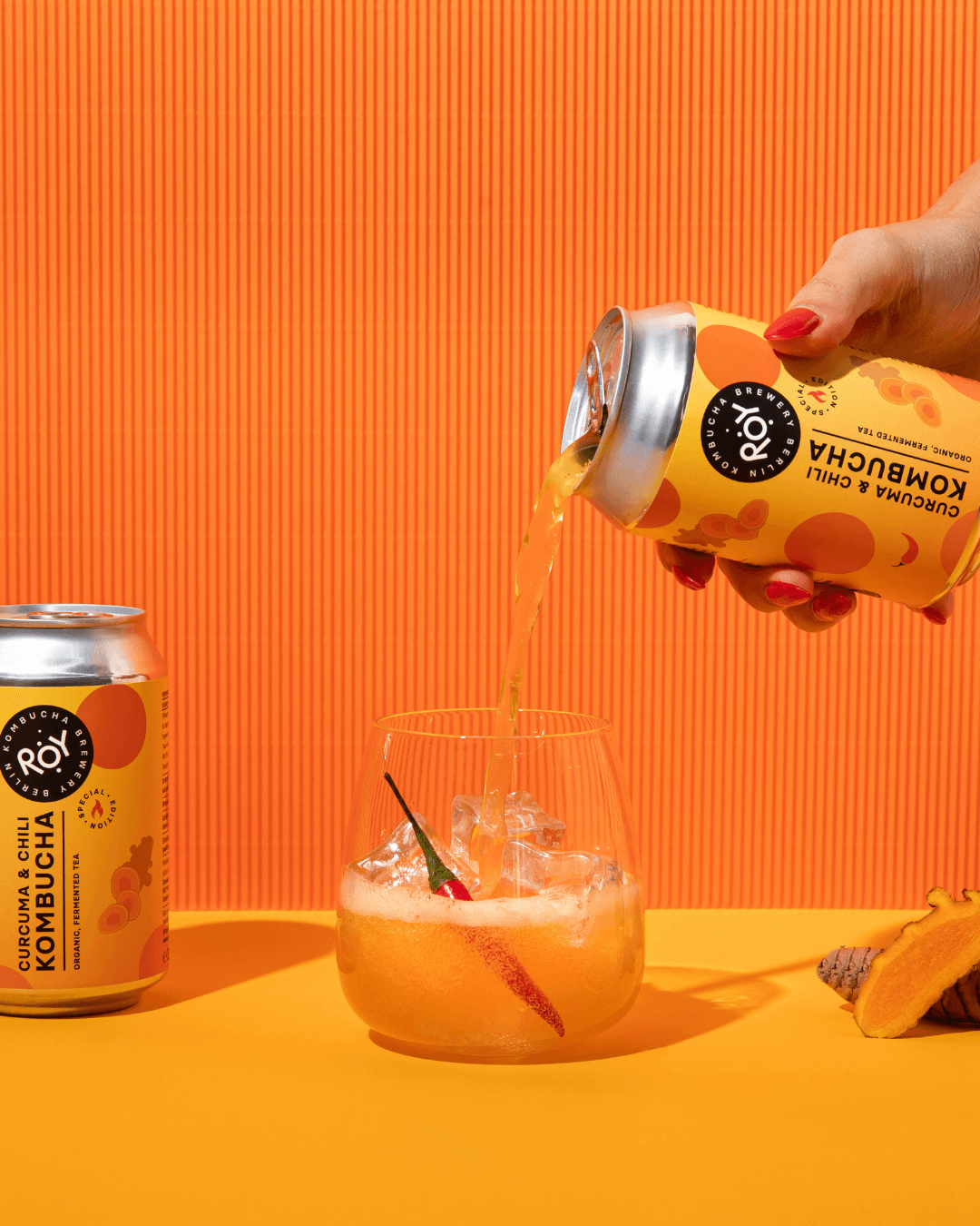 Erfrischender Kurkuma-Chili-Kombucha von ROY, stilvoll eingeschenkt mit leuchtendem Orange-Design.