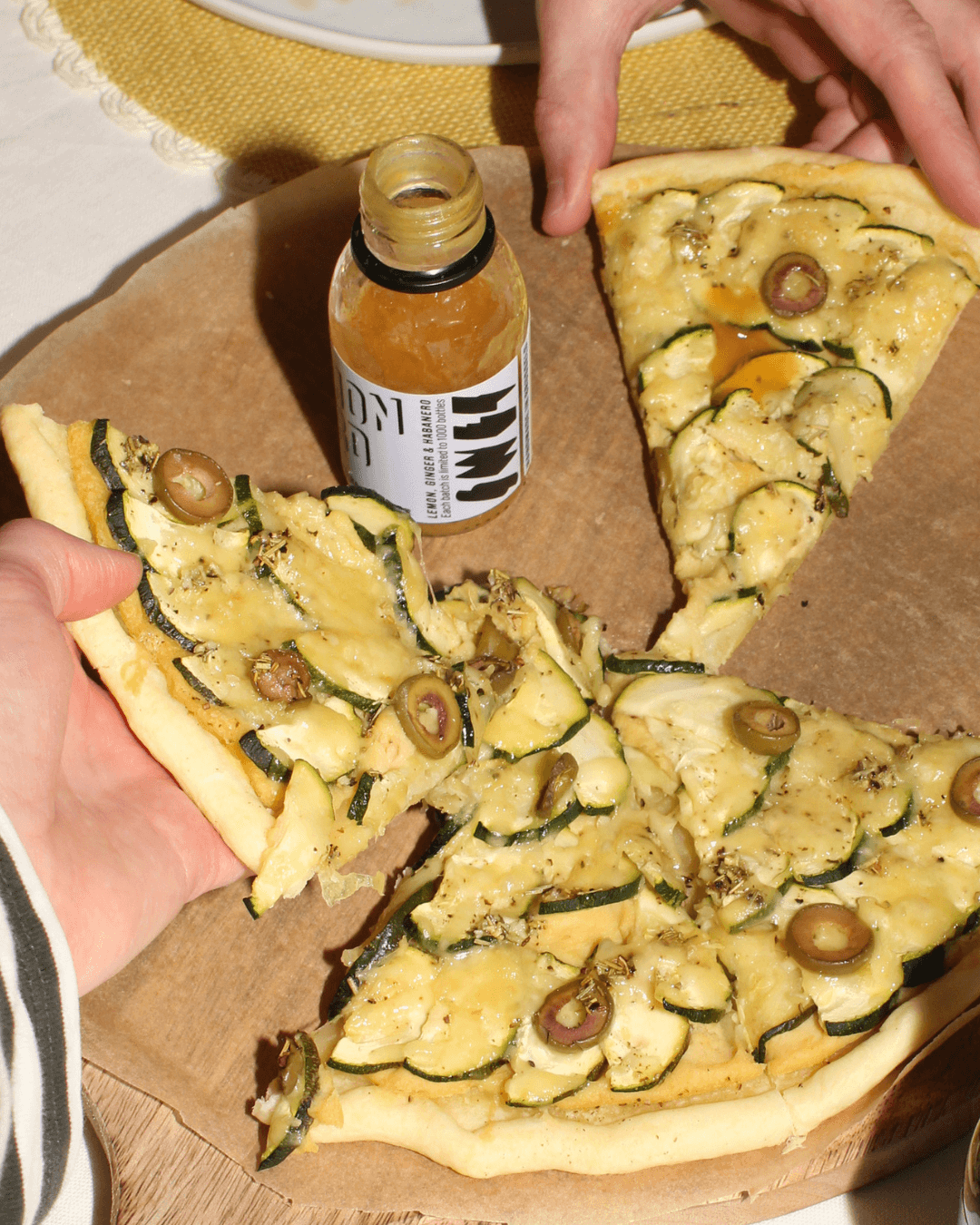 Zucchini-Oliven-Pizza mit geschmolzenem Käse, serviert mit SWET Lemon Hard Hot Sauce.