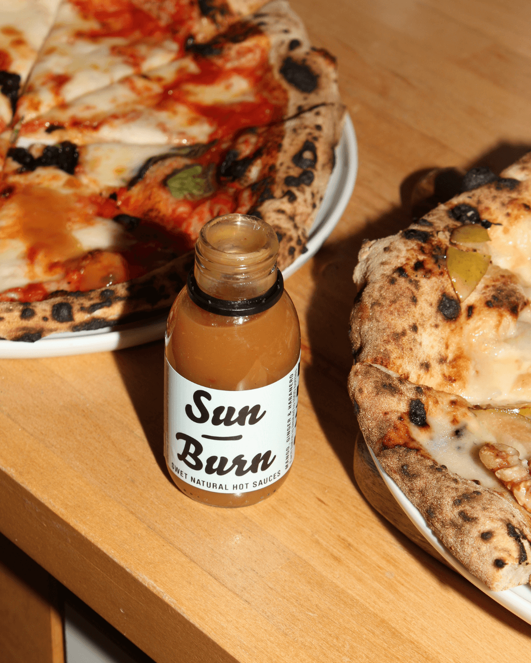 SWET Sun Burn Hot Sauce neben knuspriger neapolitanischer Pizza, verfeinert mit würziger Schärfe.