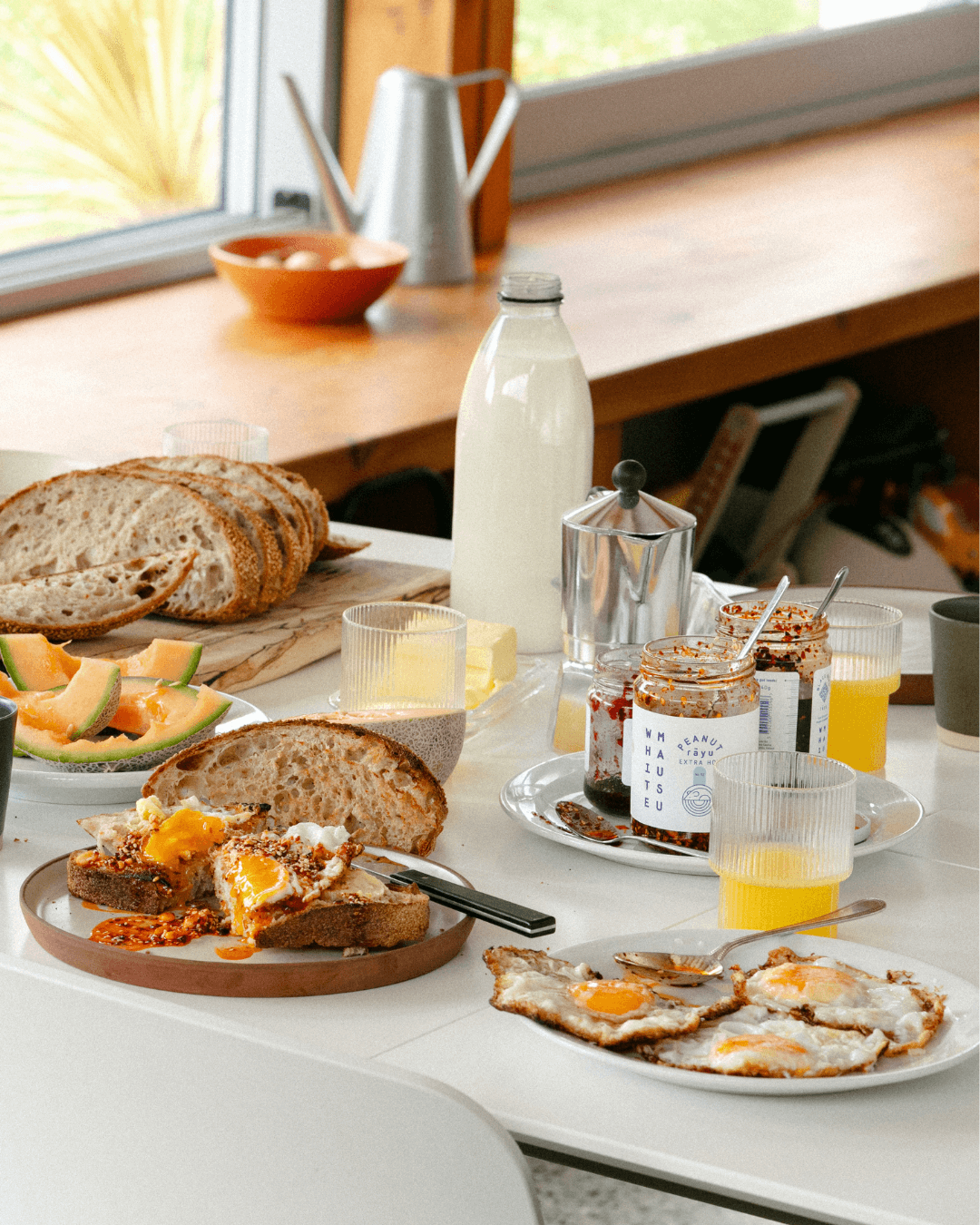 Frühstückstisch mit Brot, Eiern, Chiliöl und frischem Melonenstücken.