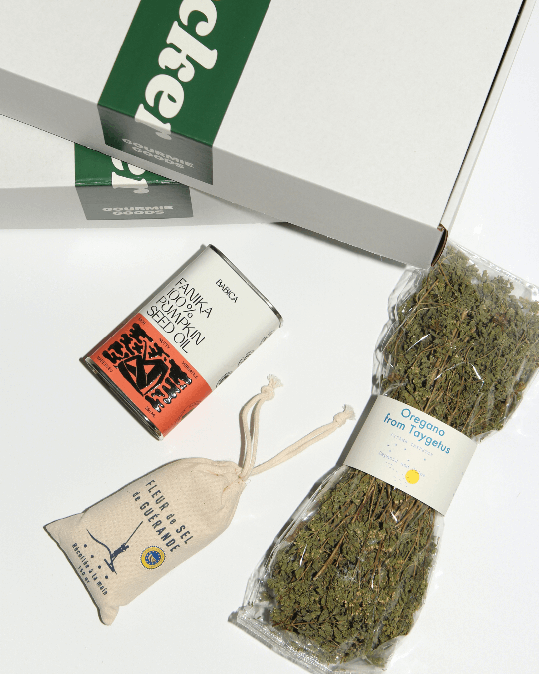 Produkte des „Chef’s Secret Stash“-Geschenksets – Fleur de Sel, Oregano und Fanika Kürbiskernöl – vor der weißen Geschenkbox.