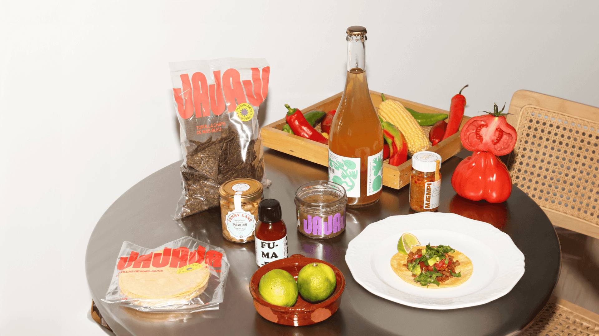 Ein Tisch mit Feinkost-Zutaten für mexikanische Küche, darunter Tortillas, Chips, Chili, Limetten, Salsa und ein Taco.