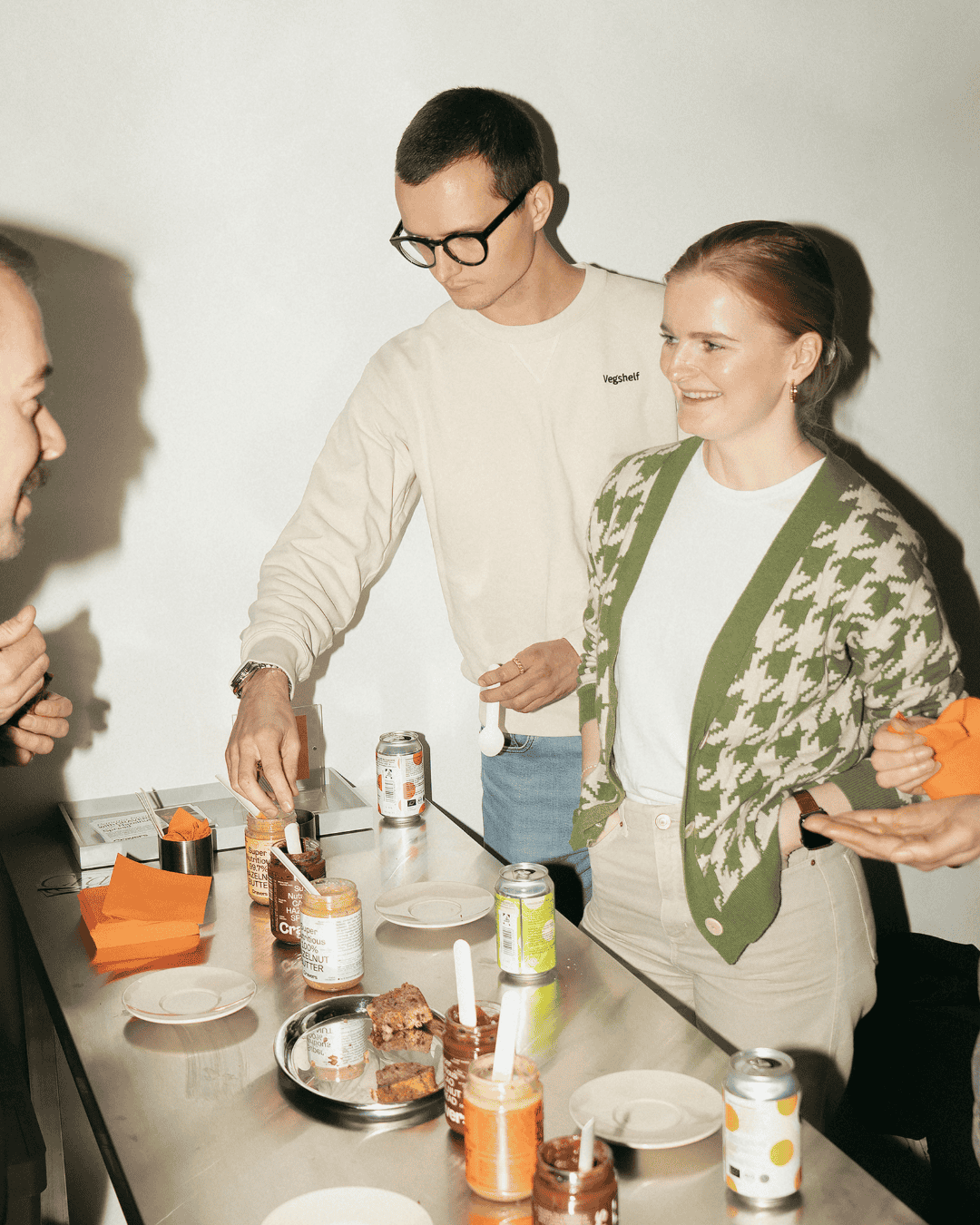 Die Gründer von Gourmie Goods genießen eine Verkostung an einem Edelstahltisch mit Brot, Aufstrichen und Getränken.