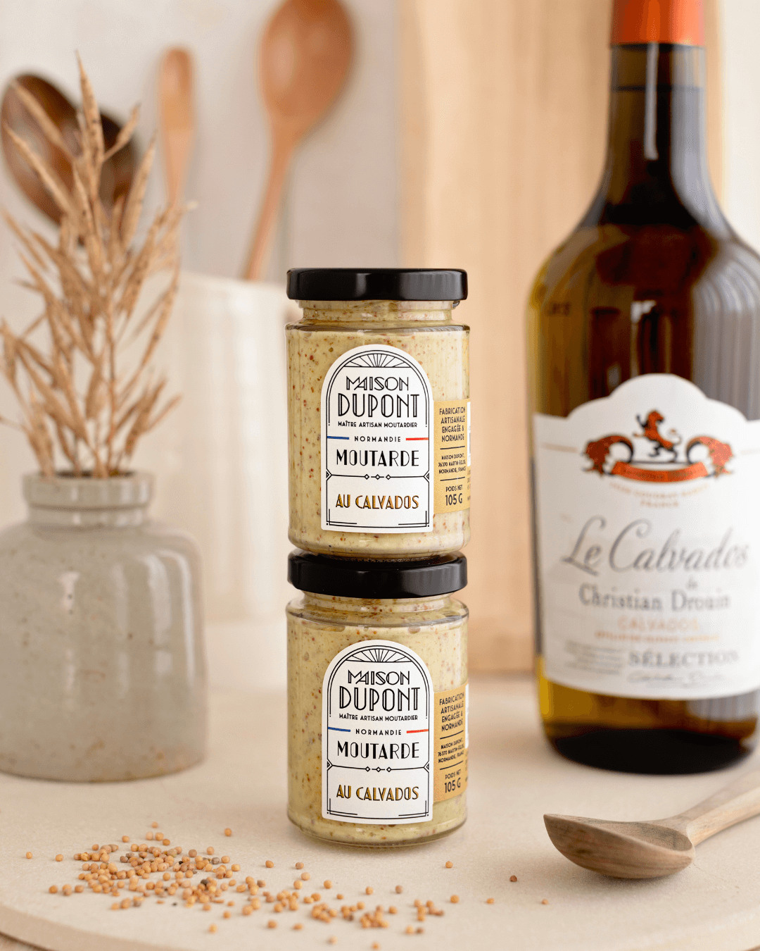 Zwei Gläser Maison Dupont Calvados Senf neben Calvados-Flasche.