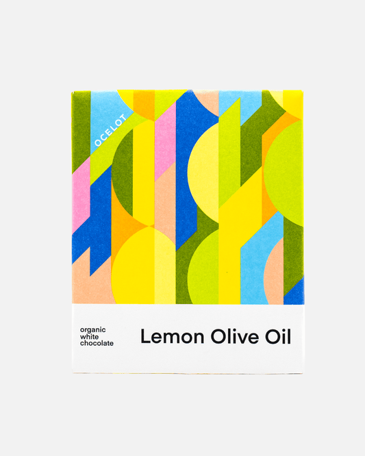 Verpackung der Ocelot Lemon Olive Oil weißen Schokolade mit einem farbenfrohen, geometrischen Design in Gelb-, Rosa- und Blau.